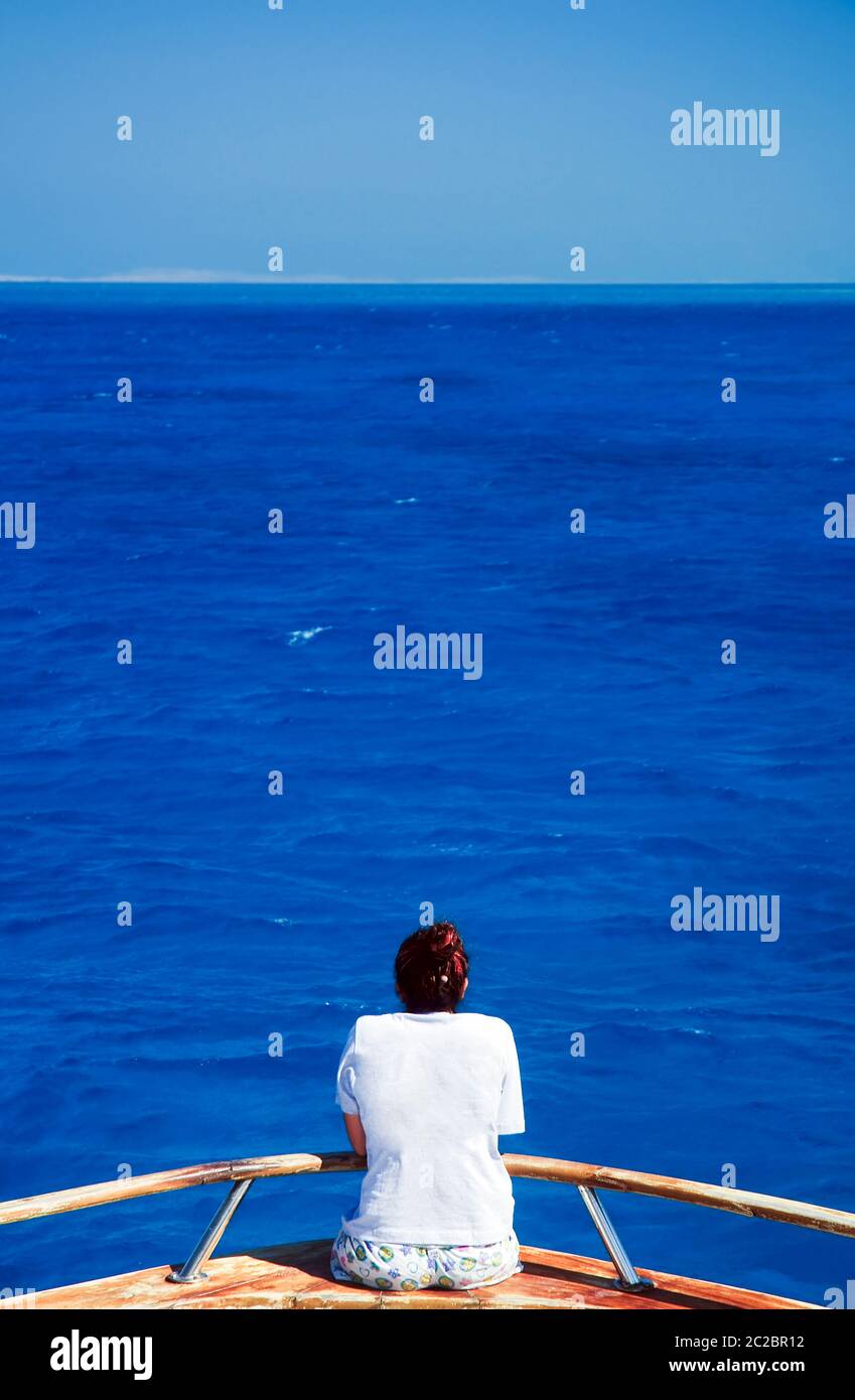 Woman in her twenties looks out at an endless expanse of calm blue ocean Stock Photo