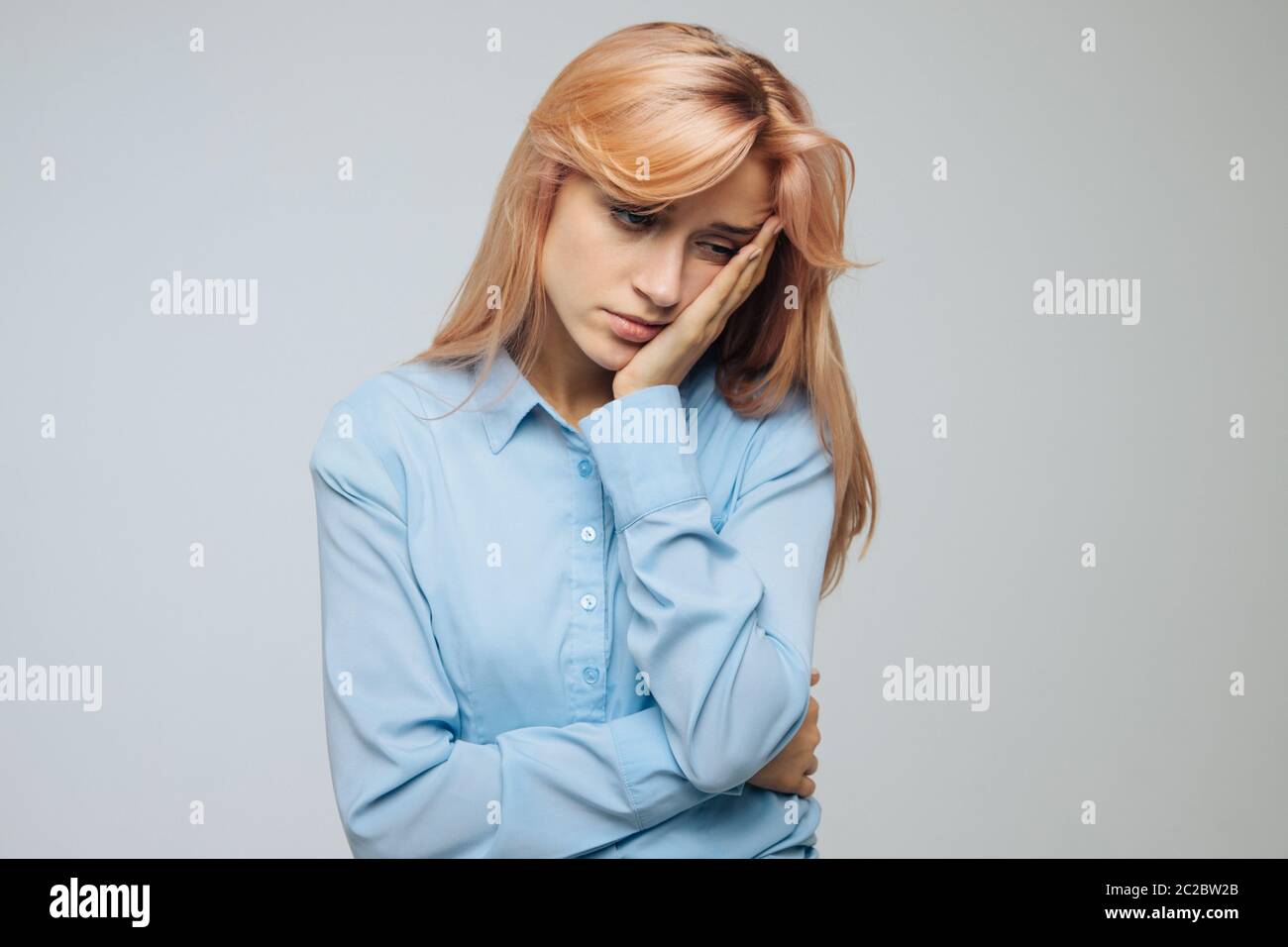 Sullen sweet young student in shirt feels apathy, sulking from sadness, leaning face on palm, closes her eyes from boredom, gazing with indifference. Stock Photo