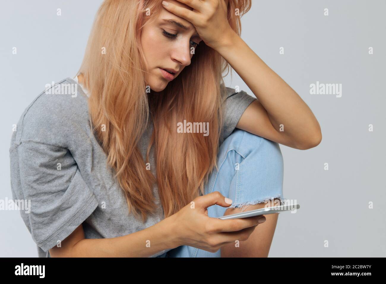 Crying young lonely woman in depression looking at phone gets bad news and touching her forehead. Problem in relationships, relationships breakup, lov Stock Photo