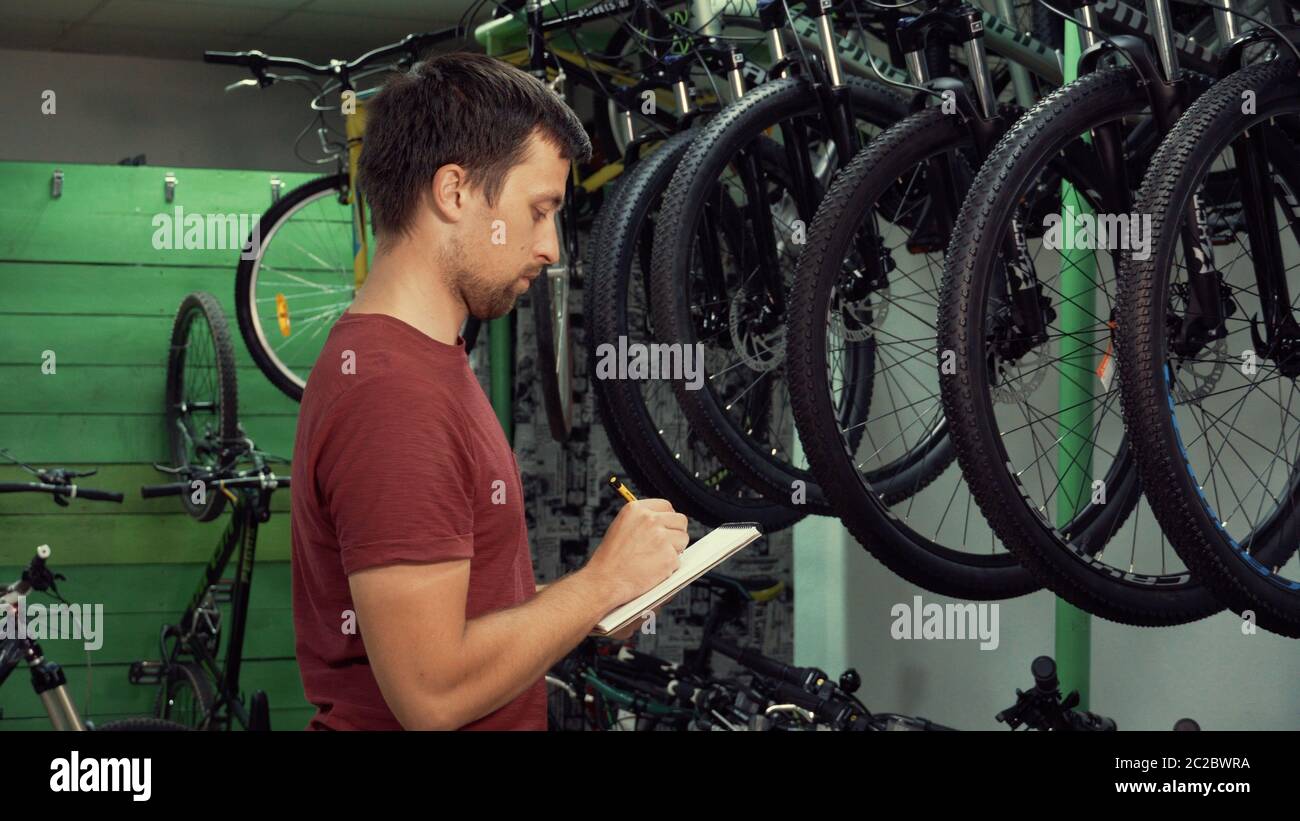 theme of small business selling bicycles. Young Caucasian male brunette small business owner, store manager uses notepad and pen Stock Photo
