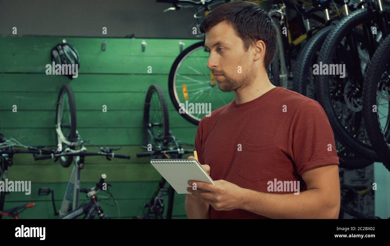 theme of small business selling bicycles. Young Caucasian male brunette small business owner, store manager uses notepad and pen Stock Photo