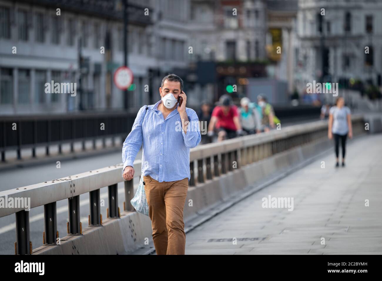 LONDON, ENGLAND - MAY 27, 2020: Middle aged Middle Eastern man walking along Waterloo Bridge in London, England wearing a face mask and talking on his Stock Photo