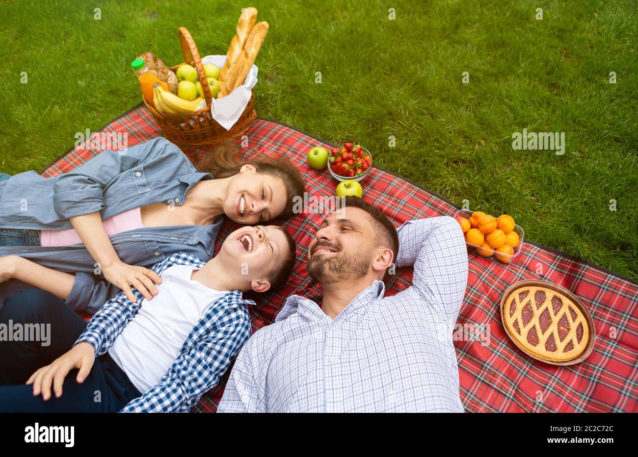 Family picnic fun. Above view of mom, dad and their son lying on checkered blanket outside Stock Photo