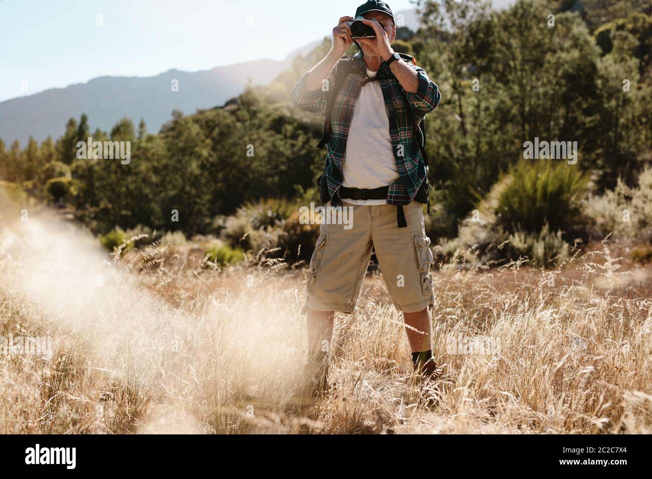 Senior man on hiking trip taking photos with a digital camera. Male hiker photographing a nature. Stock Photo