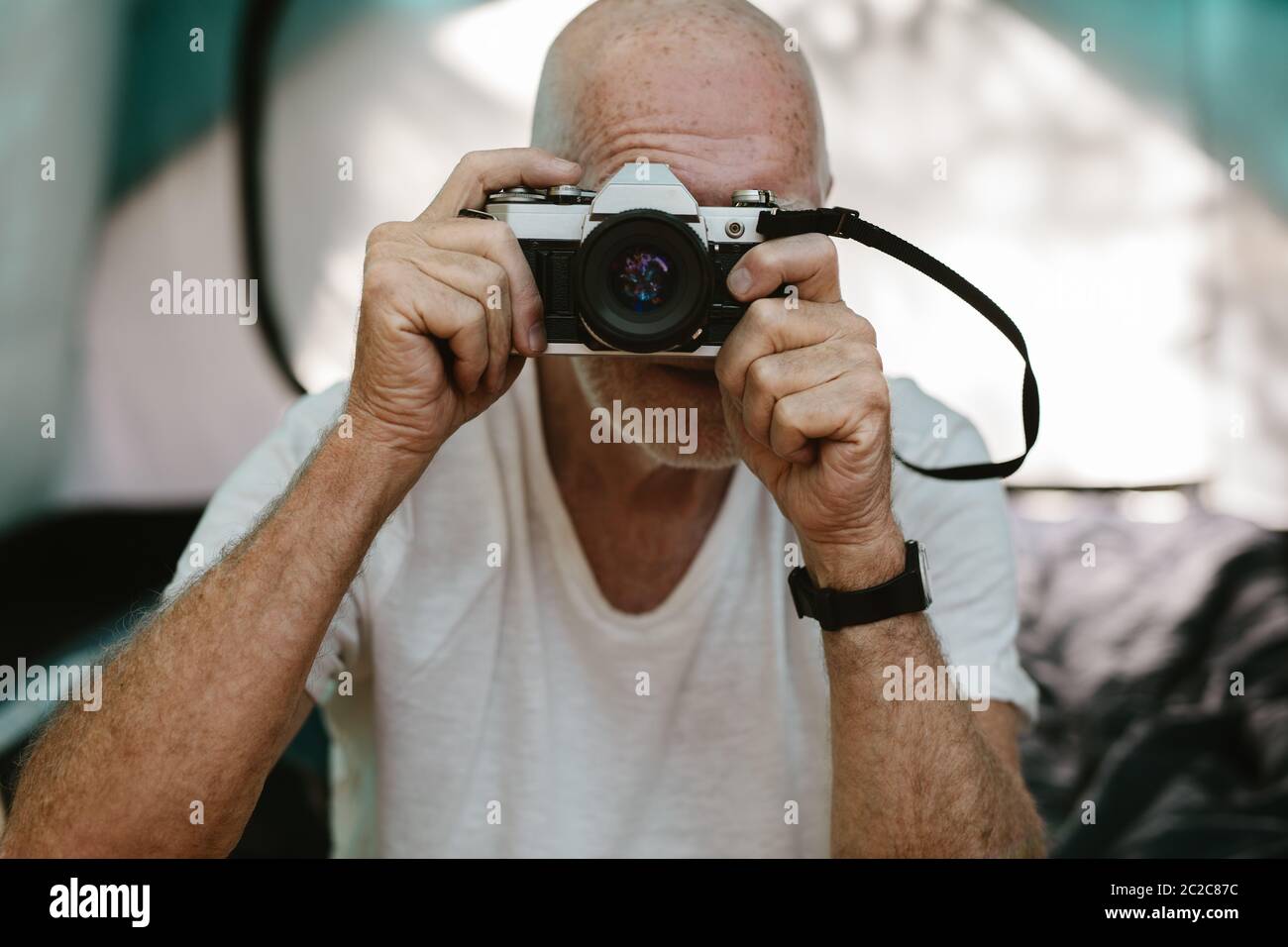 Closeup of a senior man sitting outside his camping tent and photographing with a digital camera. Retired man taking some snaps while camping in natur Stock Photo
