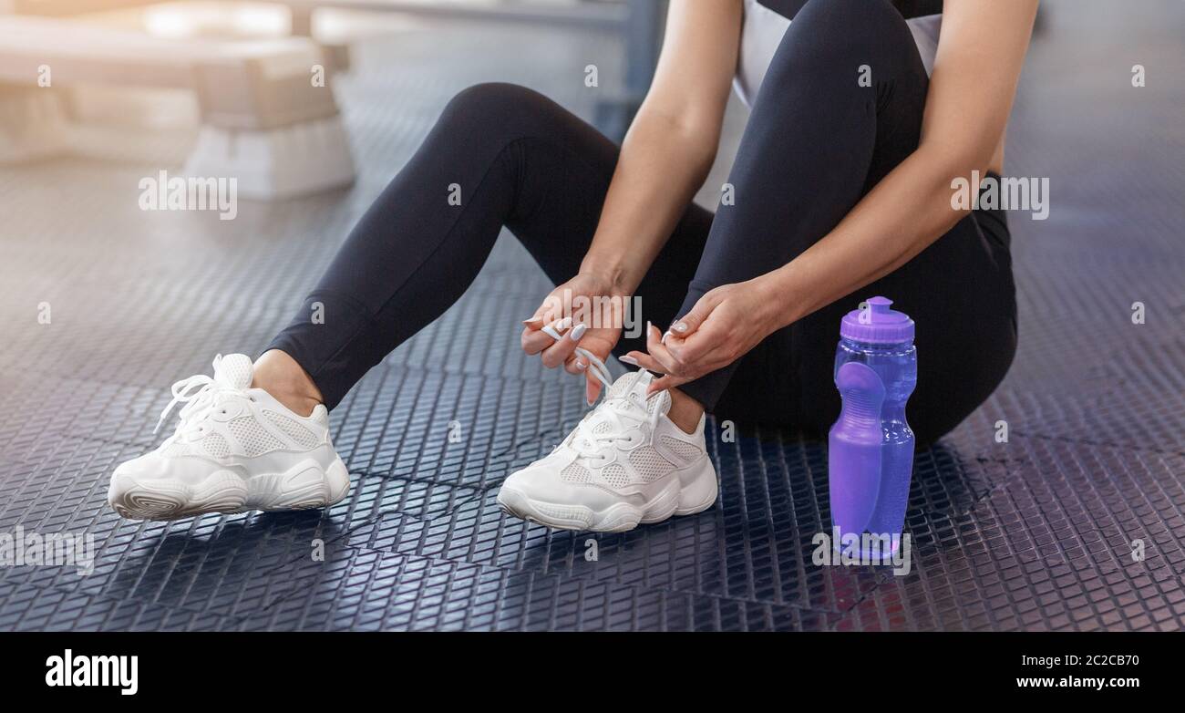 Cropped view of millennial woman tying her shoelaces on floor at fitness centre, closeup Stock Photo