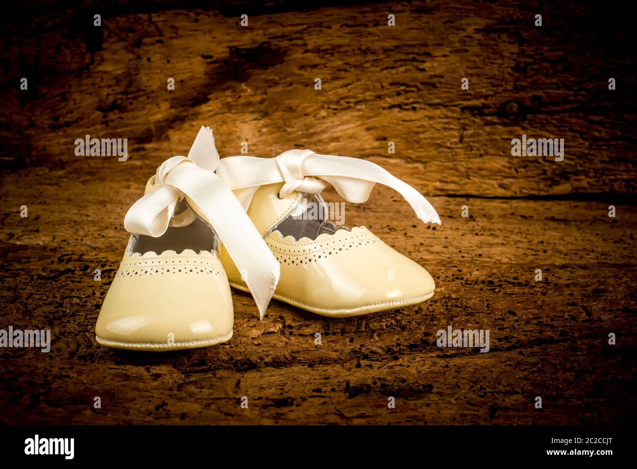 Small newborn patent leather shoes with bow on old wooden background, traditional christening wardrobe. Stock Photo