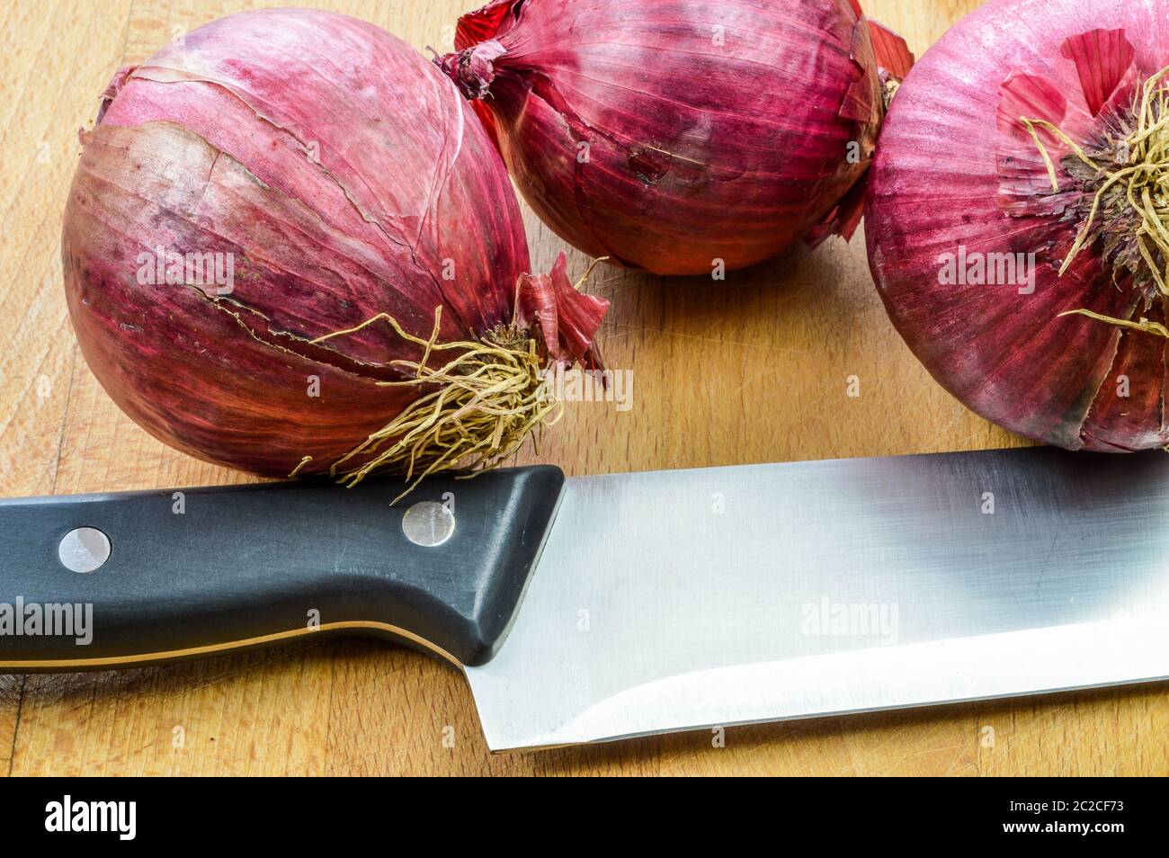 Red Onions on a wooden cutting board with kitchen knife close up ...