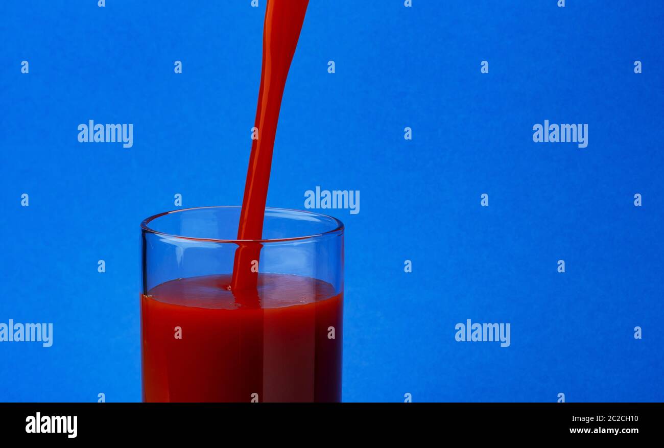 Tomato juice pouring into glass, isolated on blue background, with copy space Stock Photo