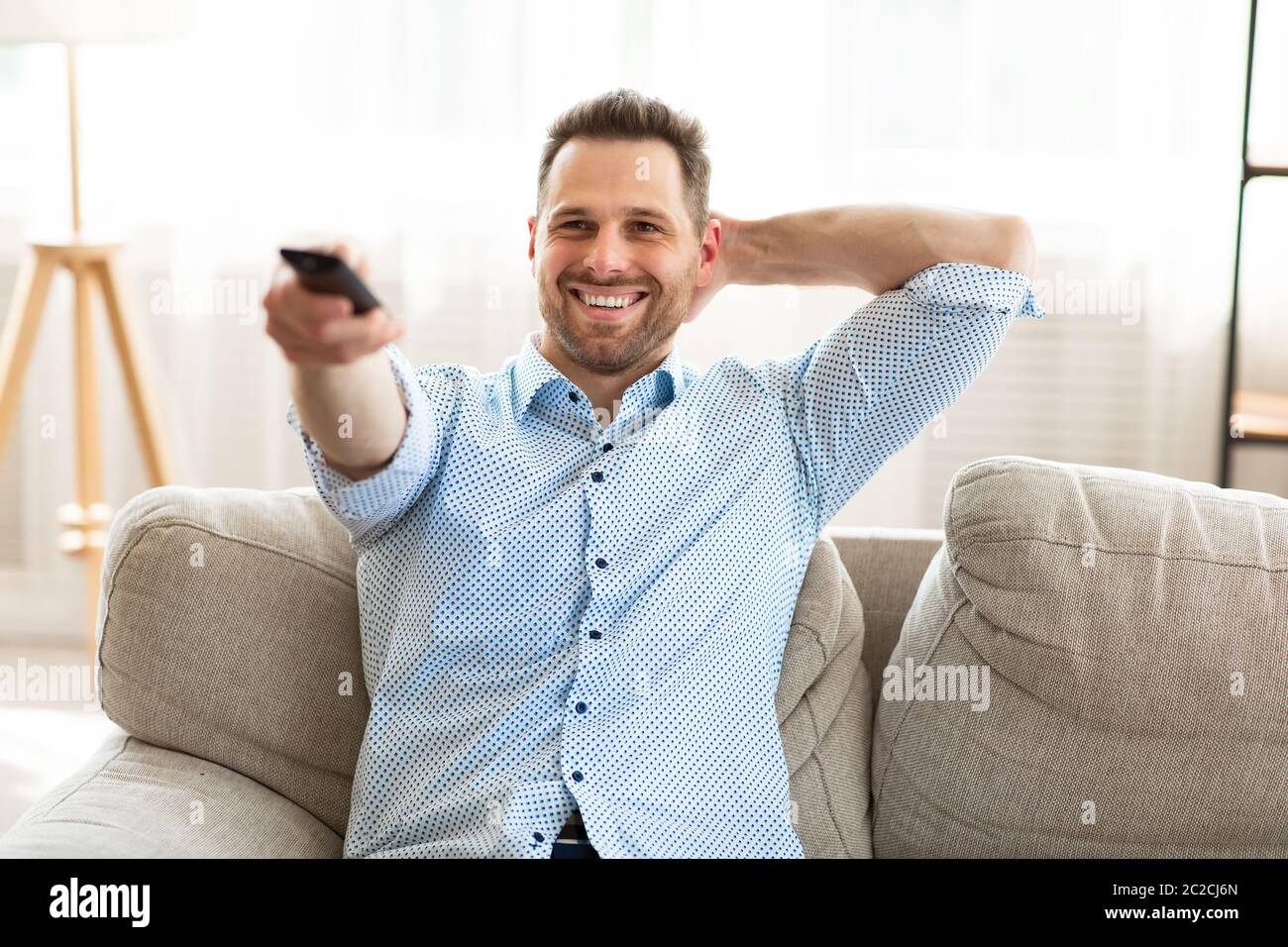 Happy guy watching TV at home, holding remote control Stock Photo