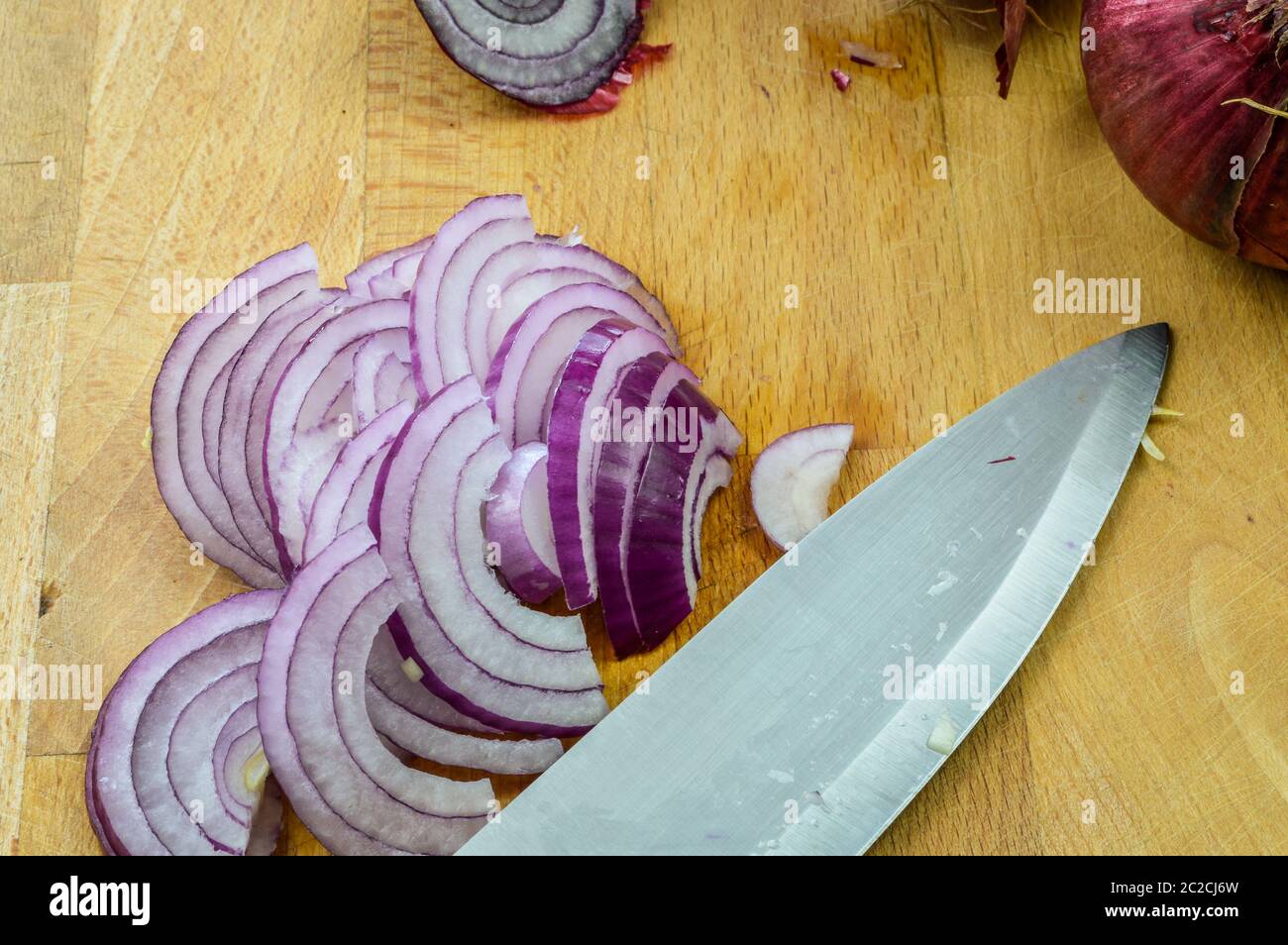 Slicing Red Onions on a wooden cutting board with kitchen knife close ...