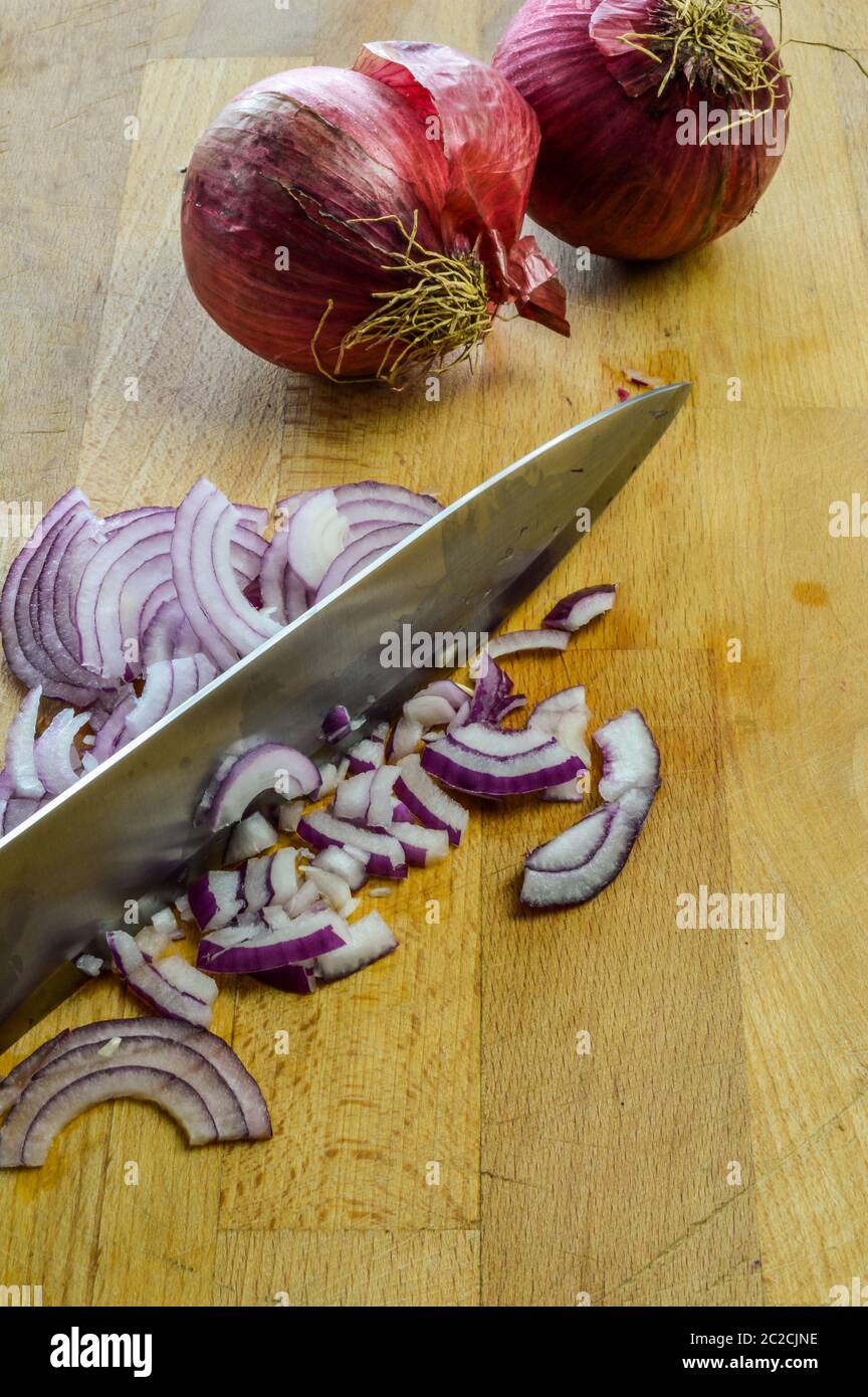 Mincing Red Onions on a wooden cutting board with kitchen knife close