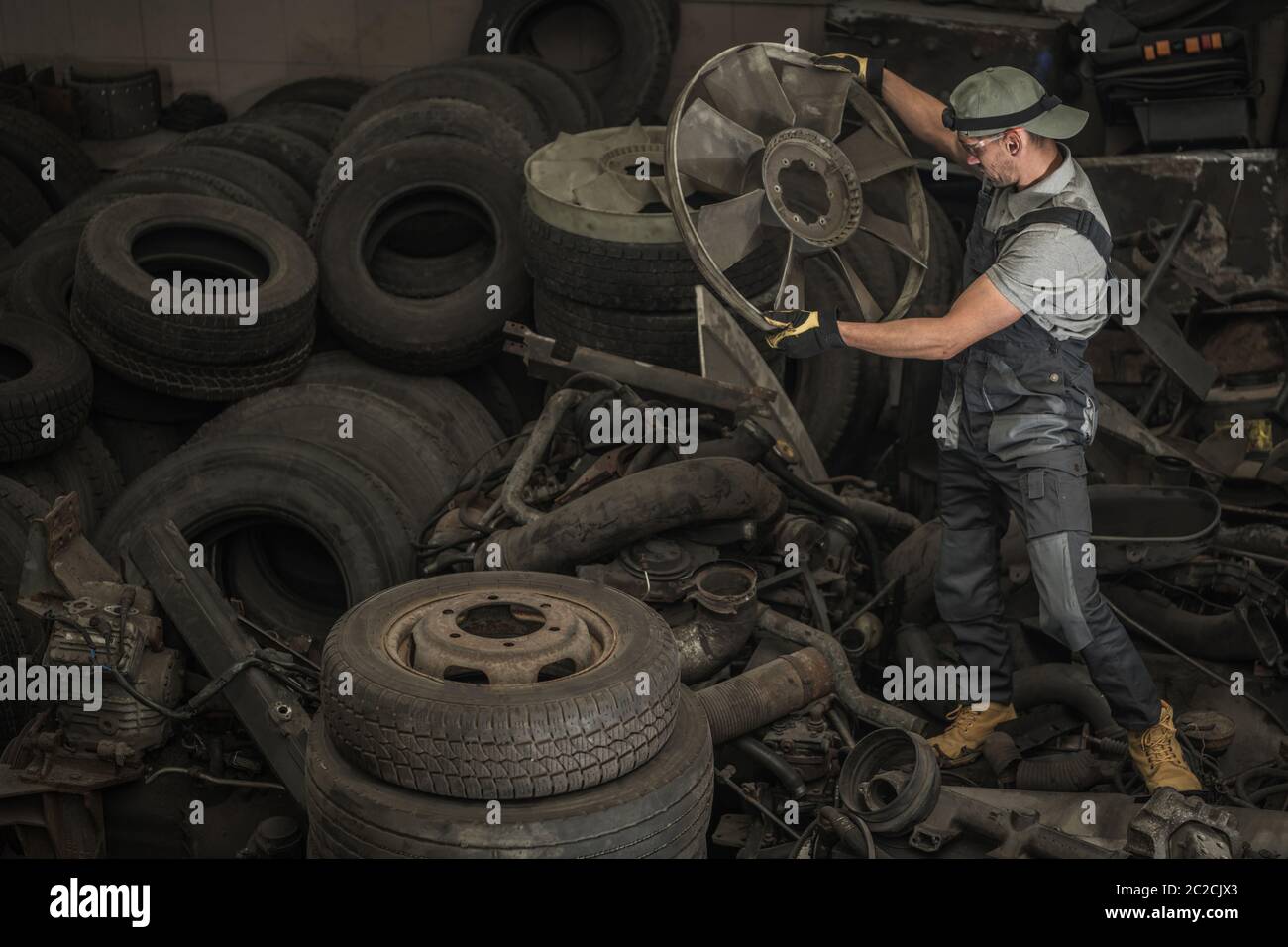 Caucasian Truck Mechanic Looking For Used Parts in Large Pile. Reusing Mechanical Elements. Bush Fix Truck and Bus Service. Stock Photo