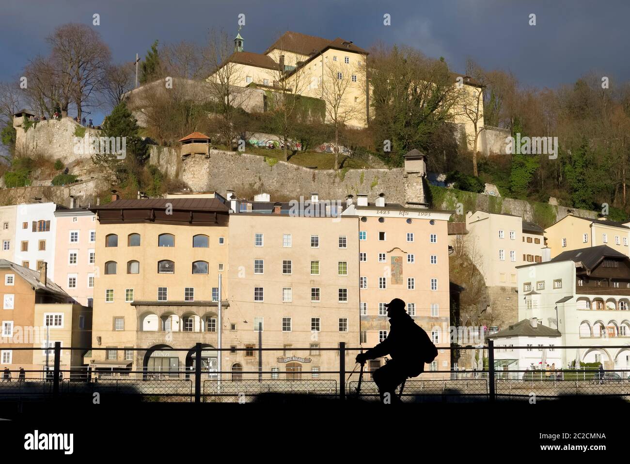 View of the Capuchin Monastery in Salzburg including the surrounding houses from the street across the river with a silhouette of cyclist. Stock Photo