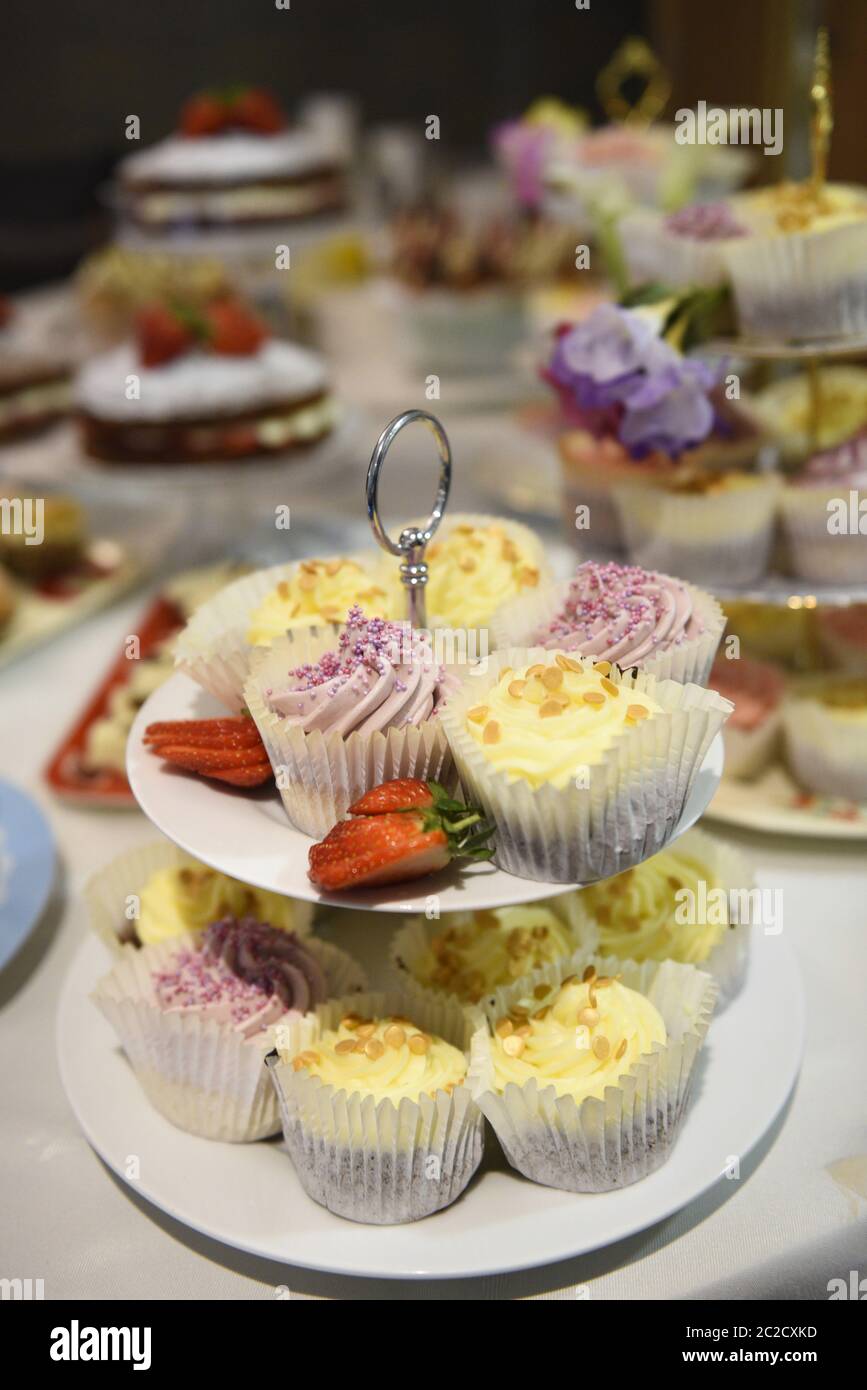 Fancy cakes on a cake stand at a buffet. Selective focus. Real life selection of tea and fairy cakes at a party celebration. Stock Photo