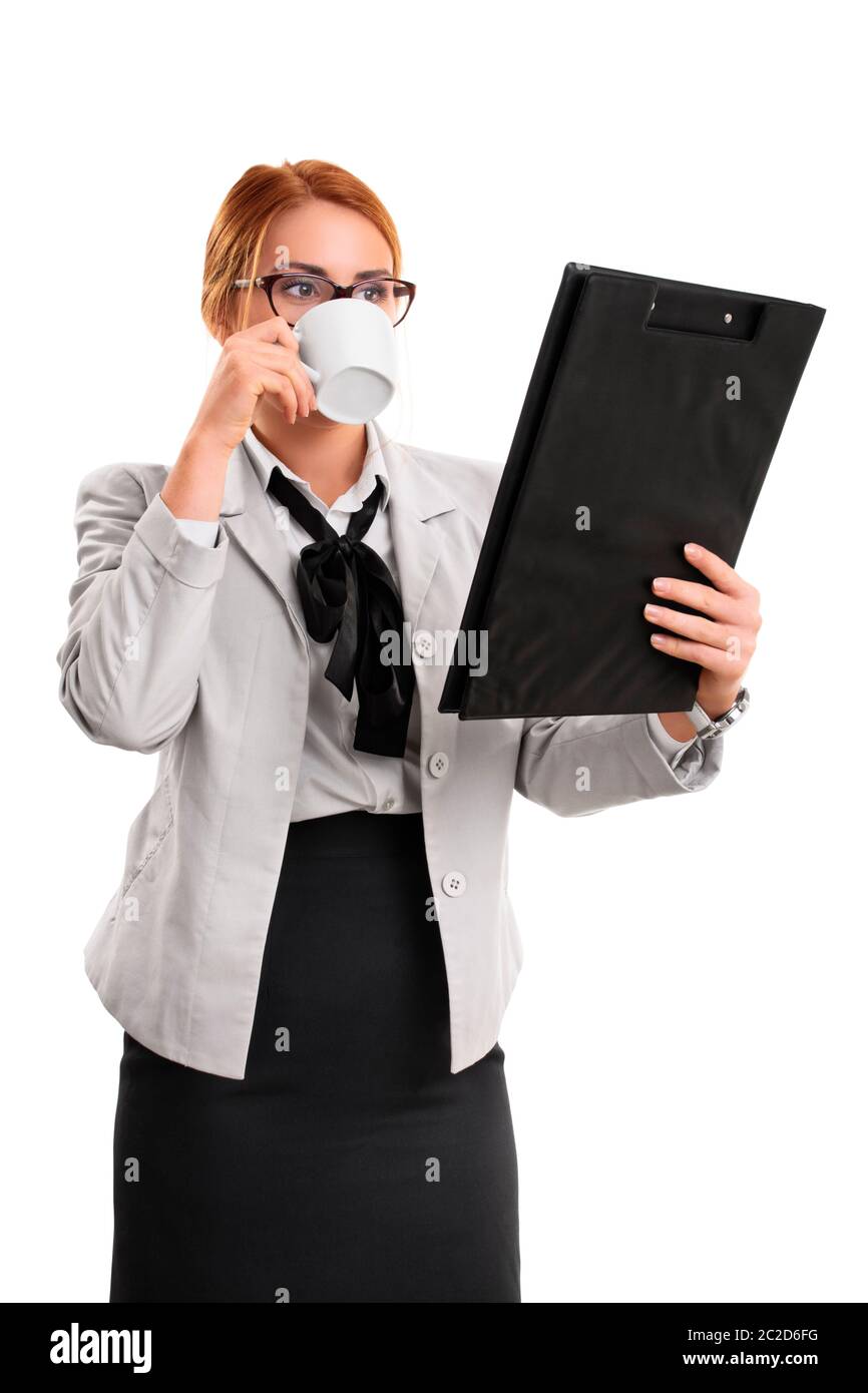 A portrait of a businesswoman drinking from a cup and looking at a clipboard, isolated on white background. Stock Photo