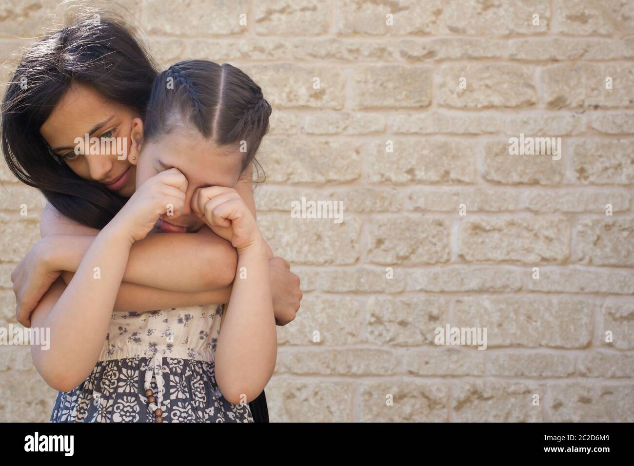 An older girl supports a young girl who is crying Stock Photo