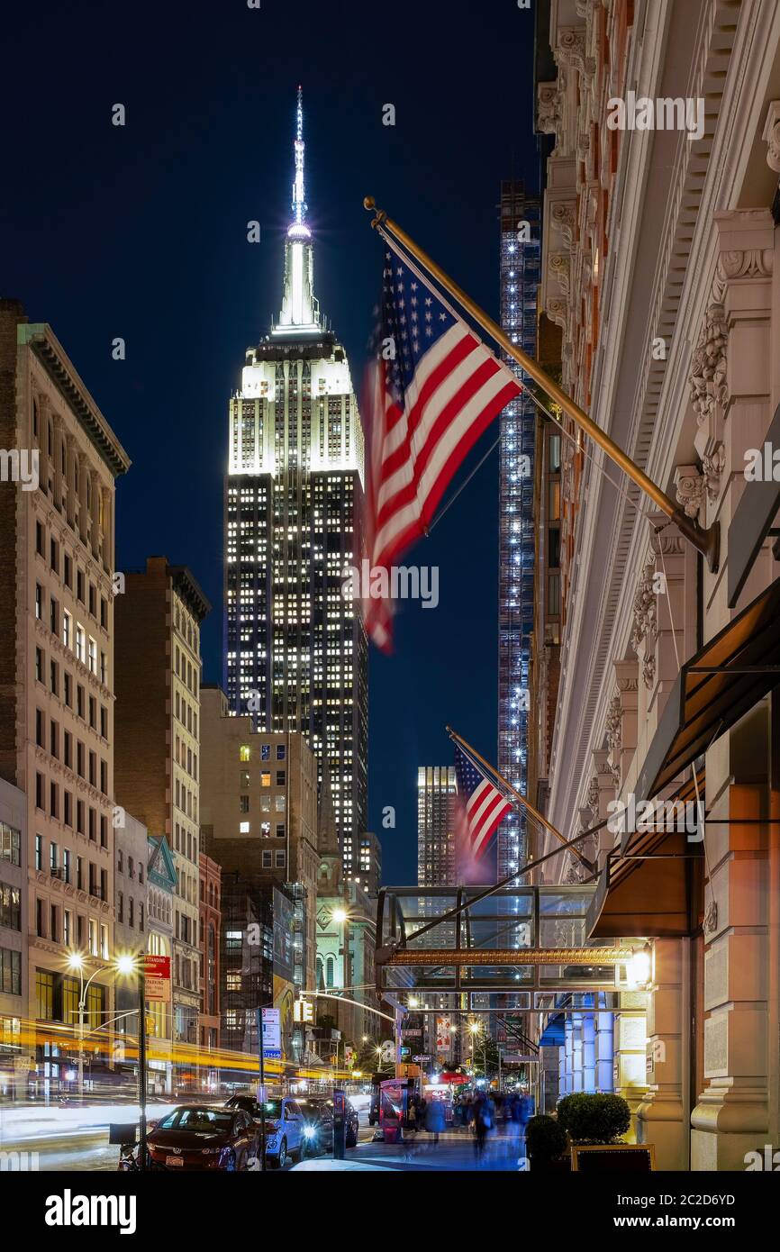Street view of Empire State Building at dusk with traffic, people and flag Stock Photo