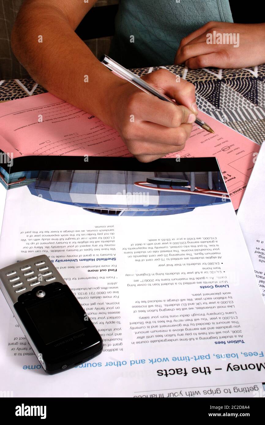 Young person completing university application & student loan forms, old Nokia mobile phone is lying on table Stock Photo