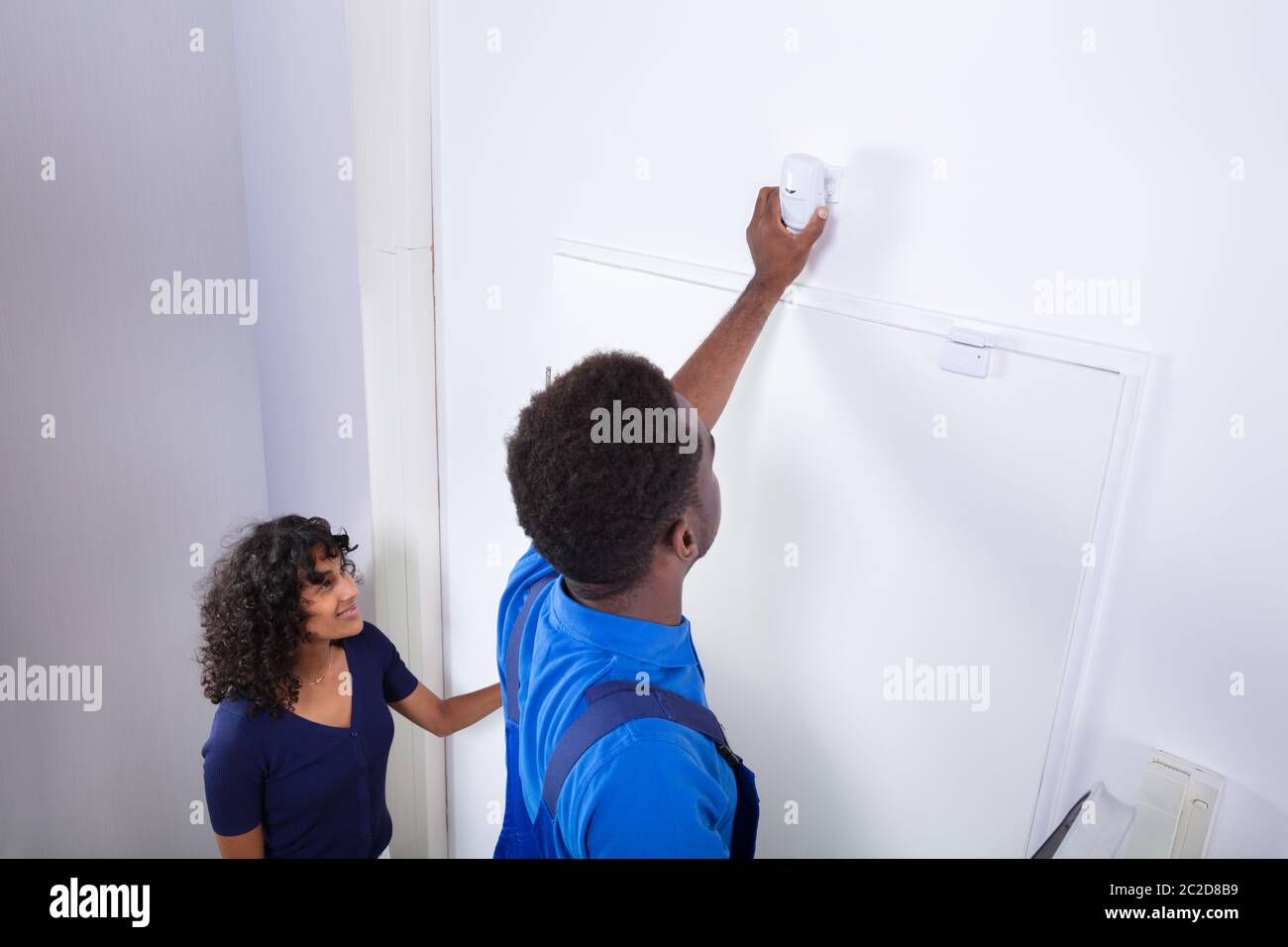 Electrician Installing Security System Motion Detector On Wall Stock Photo