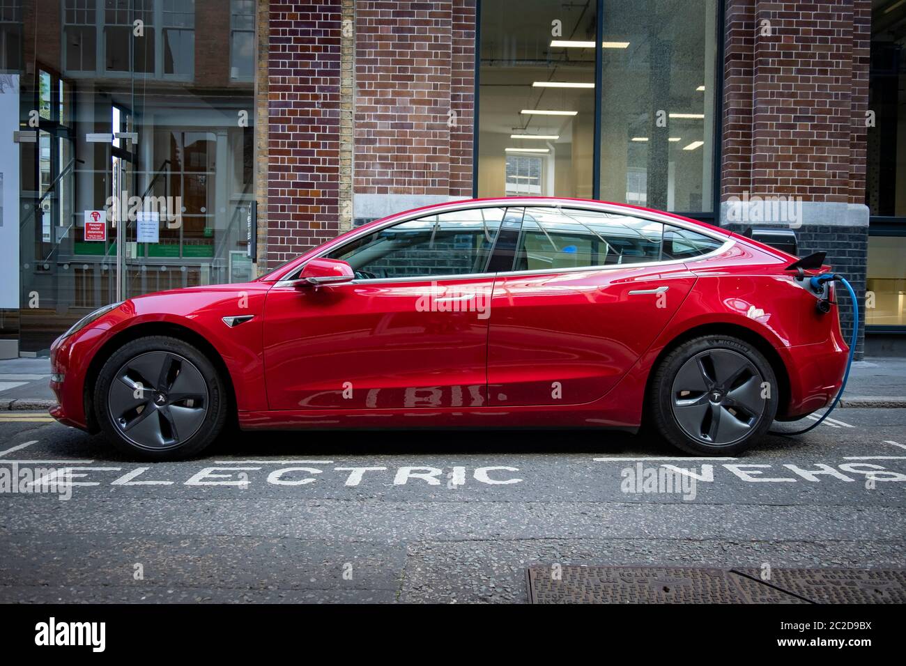 LONDON, JUNE, 2020: A red Tesla Model 3 parked and charging on city street Stock Photo