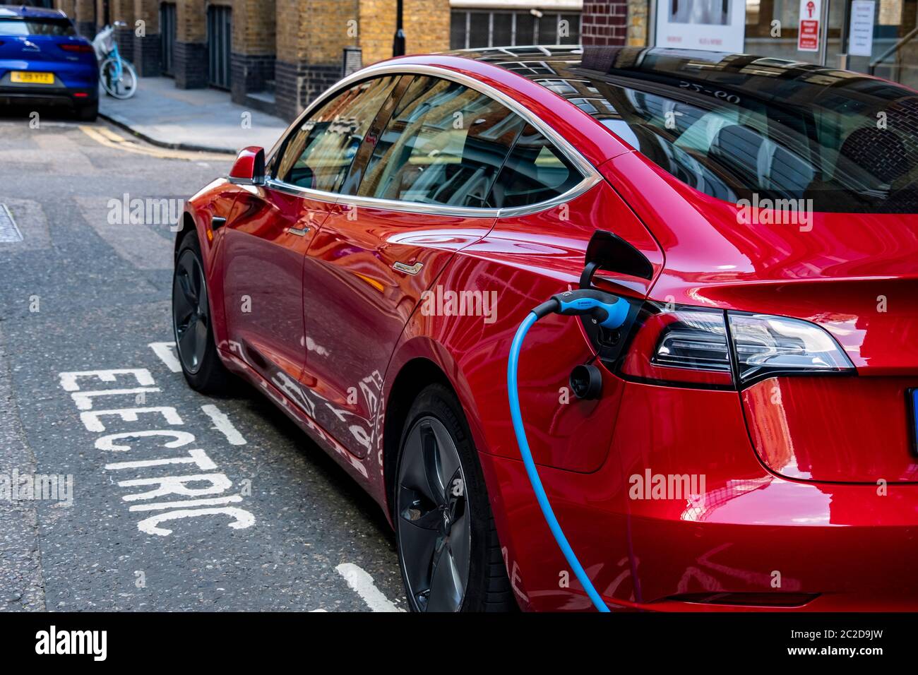 LONDON, JUNE, 2020: A red Tesla Model 3 parked and charging on city street Stock Photo