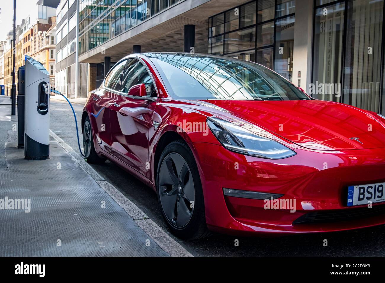 LONDON, JUNE, 2020: A red Tesla Model 3 parked and charging on city street Stock Photo