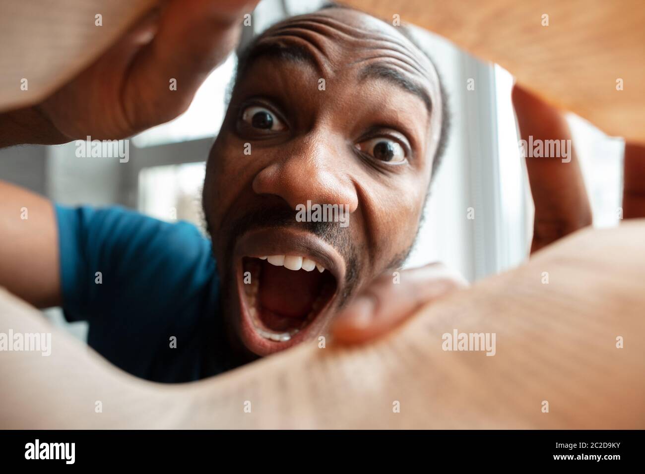 In papers, magazines, books. African-american man looking for job in unusual places at his home. Crazy, funny way to find career and going up. Concept of crisis, unemployment, finance, business. Stock Photo
