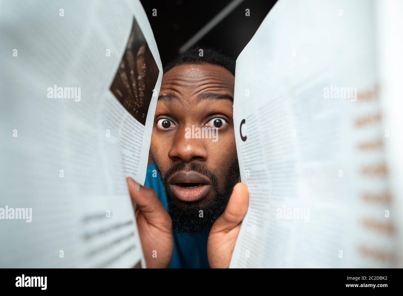 In papers, magazines, books. African-american man looking for job in unusual places at his home. Crazy, funny way to find career and going up. Concept of crisis, unemployment, finance, business. Stock Photo