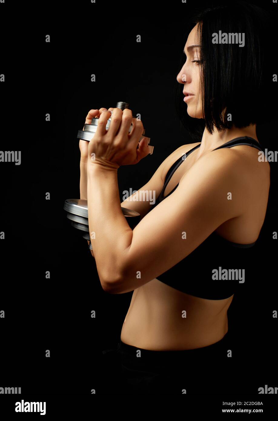 https://c8.alamy.com/comp/2C2DGBA/young-woman-of-caucasian-appearance-holds-steel-type-setting-dumbbells-in-her-hands-sports-training-dark-background-2C2DGBA.jpg