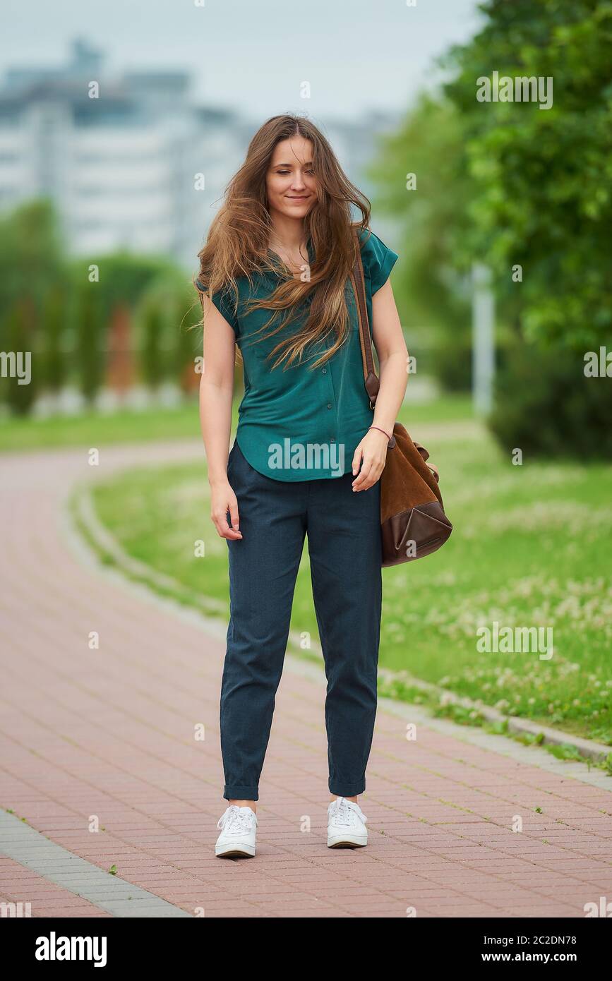 A young woman wears stylish casual clothes shakes her head to blow her hair in the park. A girl with long hair wears office style clothes Stock Photo