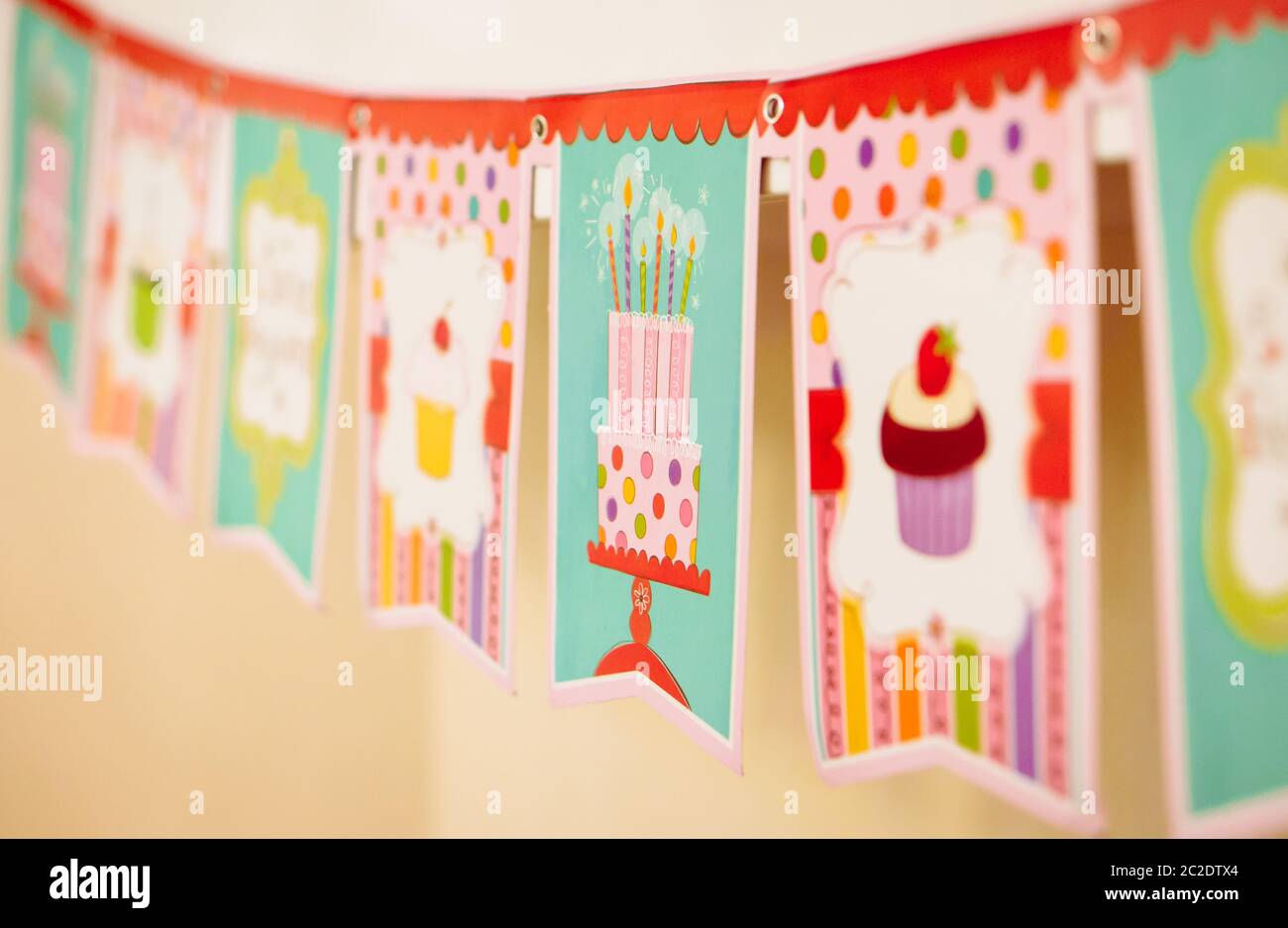 Close view of colorful birthday flags, garland with images of cake, candles. Stock Photo