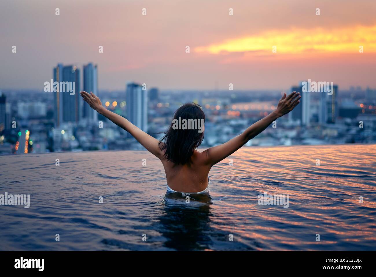 Back view of happy freedom woman with raised arms enjoy her summer vacation on swimming pool Stock Photo