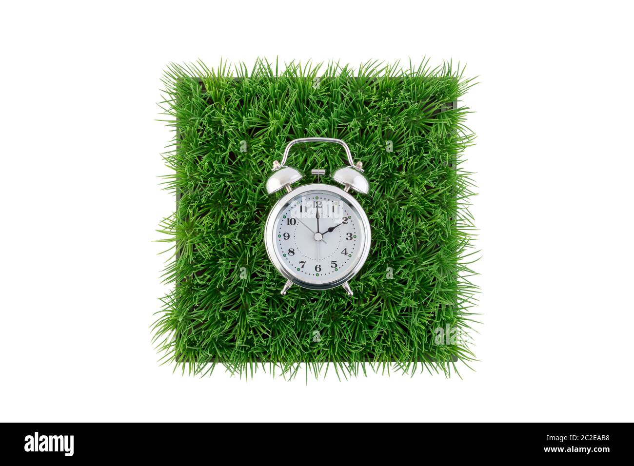 Old style alarm clock on square of green grass field isolated on white ...