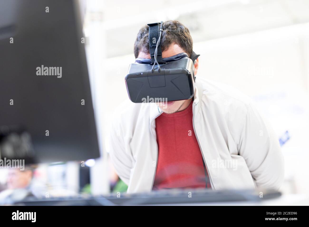 Young man wearing virtual reality headset and gesturing while sitting at his desk in creative office. Virtual reality in video games. Stock Photo