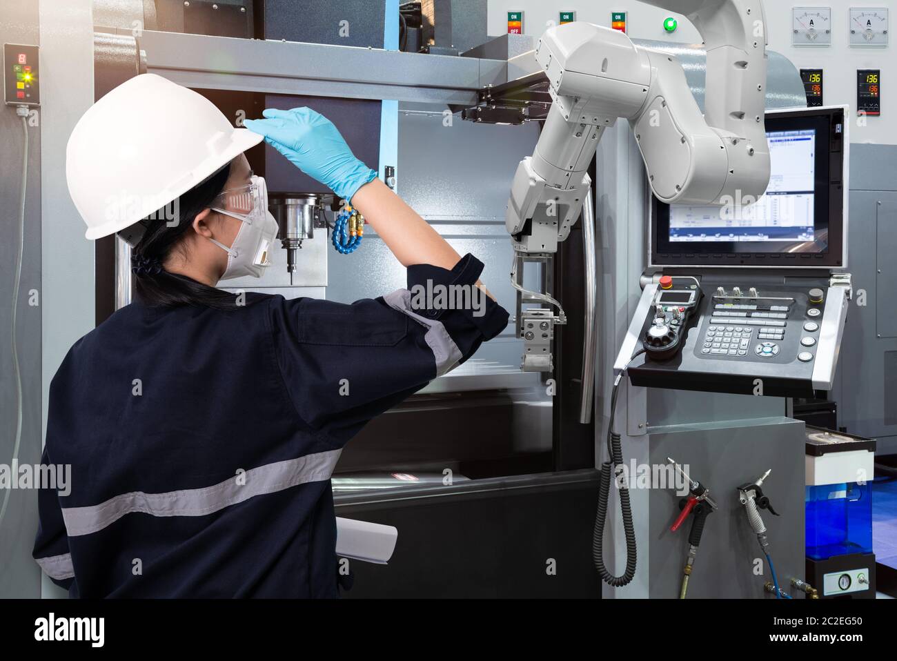 Female engineer wearing protective mask and glove to protect against Covid-19 and looking at robot CNC machine in smart factor Stock Photo