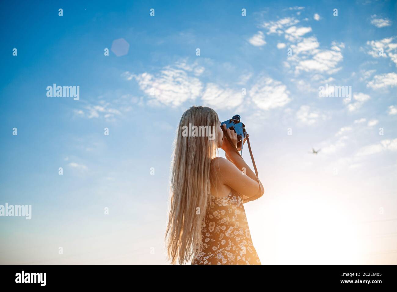 portrait of a blonde girl in a floral print dress with a vintage video  camera in a grape field records video of a plane taking o Stock Photo -  Alamy