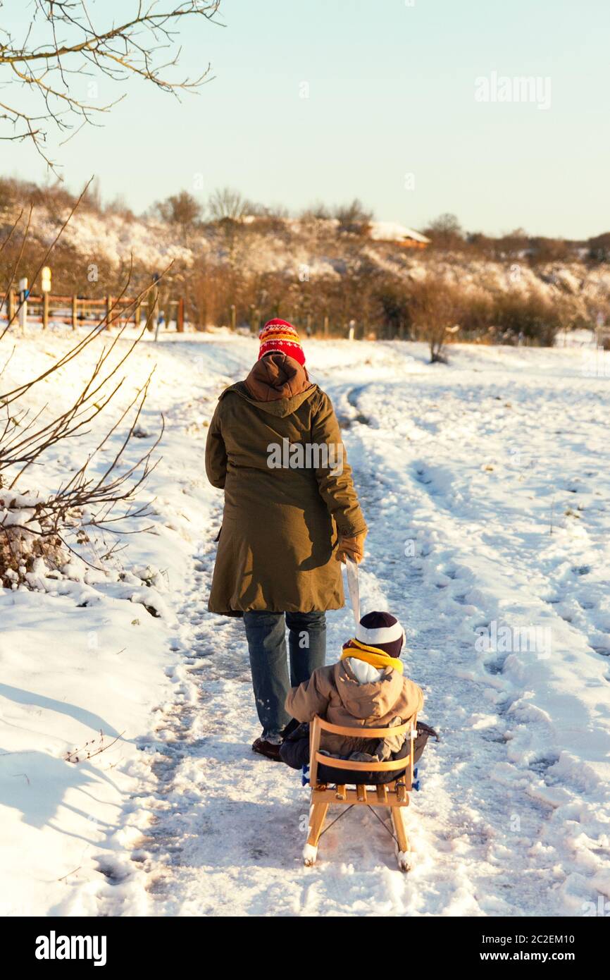 Little toddler walking outdoors in a snowy winter scene with his mom. Stock Photo