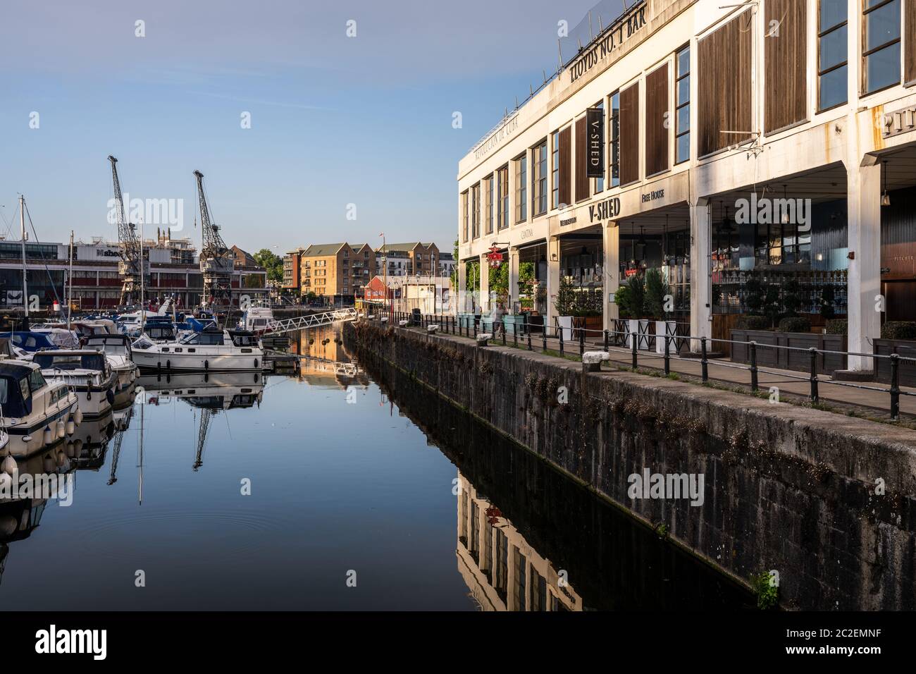 Joggers run on Bristol's Harbourside beside V Shed, one of several historic transit shed warehouses converted into bars and restaurants. Stock Photo