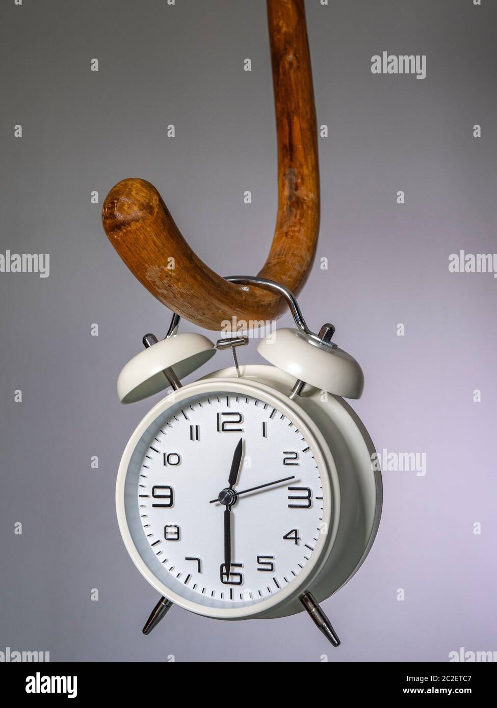An alarm clock hanging from a wooden walking cane -  a time related concept in relation to elderly people. Stock Photo