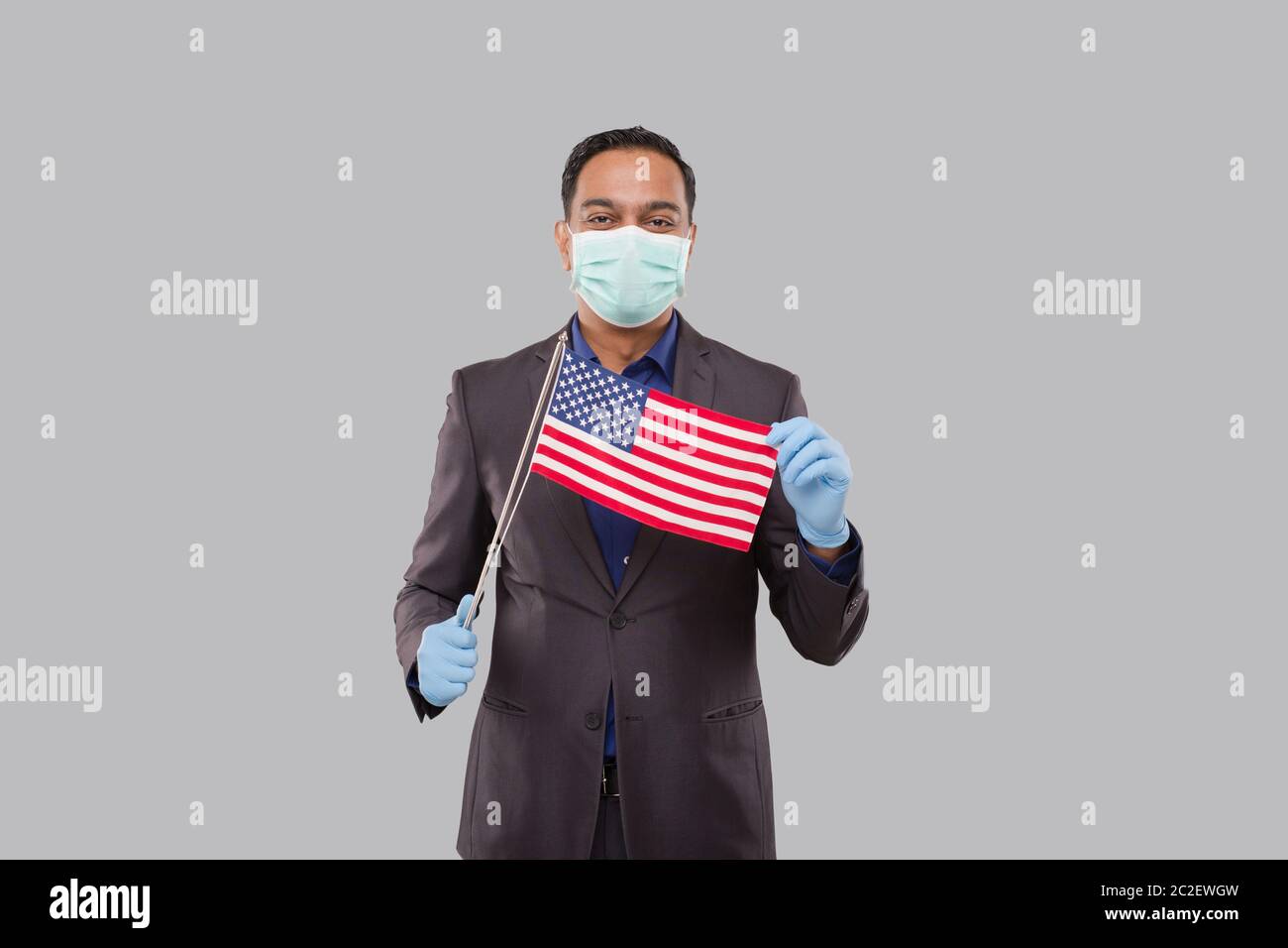 Businessman Holding American Flag Wearing Medical Mask and Gloves. Indian Businessman Standing Full Length with USA Flag in Hands Stock Photo