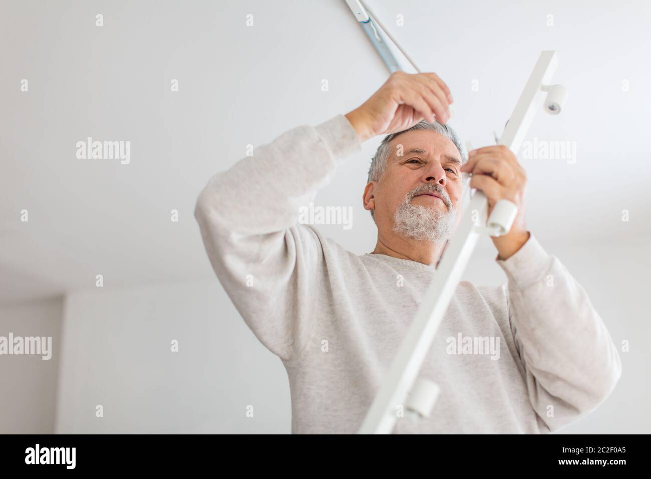 Senior man installing a ceiling light n a freshly renovated appartment ...