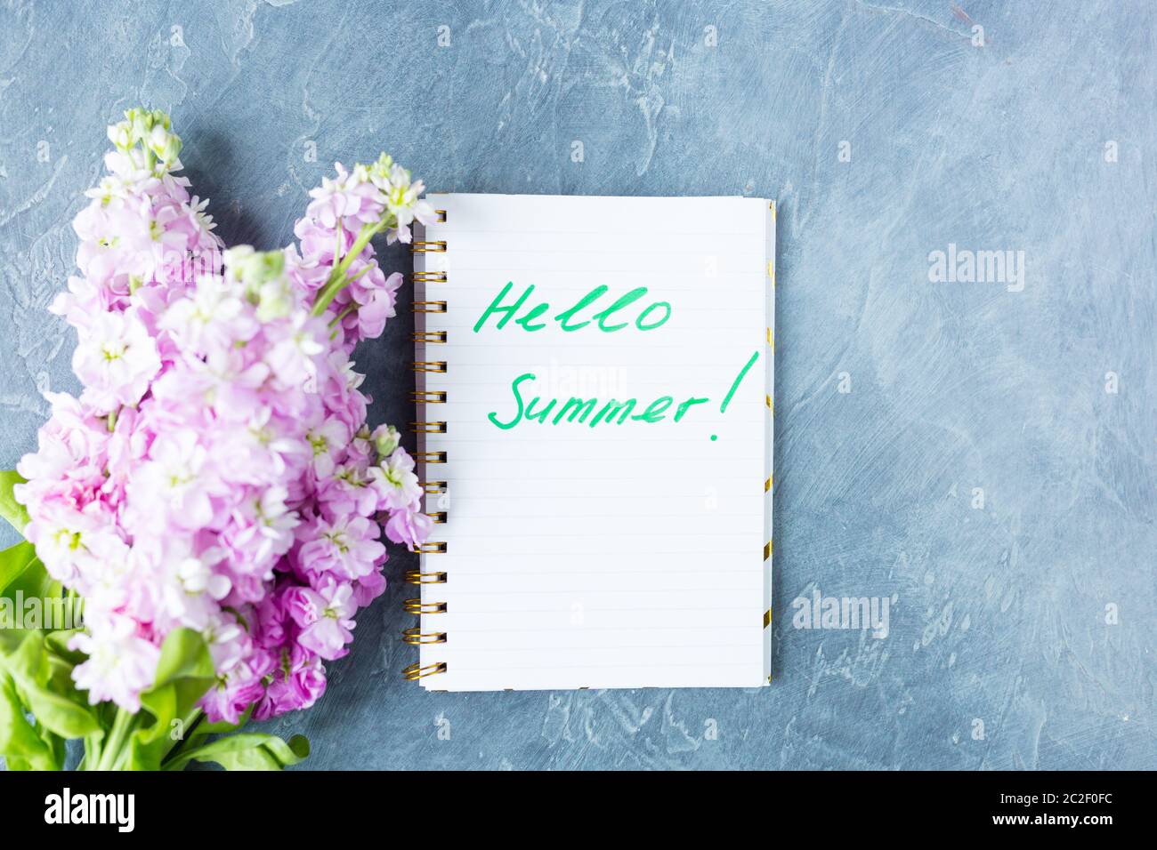 Desk top view. Phrase words Hello Summer. Purple flowers top view, flat lay. Copy space. Stock Photo