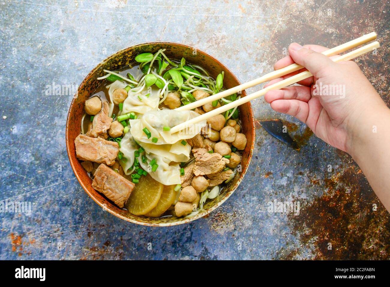 Wonton soup with meat balls, spring onion served in a big brown bowl, selective focus Stock Photo