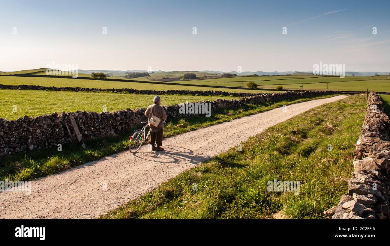 A leisure cyclist pauses to take in the view on a gravel track, part of the National Cycle Network, near Hartington in Derbyshire's Peak District. Stock Photo