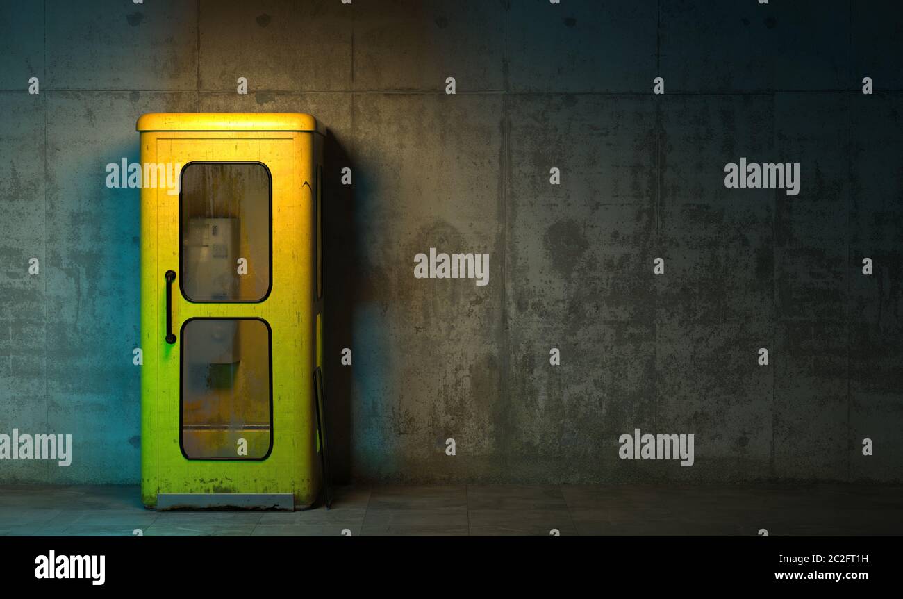 Single old yellow phone booth in retro style standing on the floor in front of the concrete wall at night time. Gloomy poorly lit interior in loft sty Stock Photo