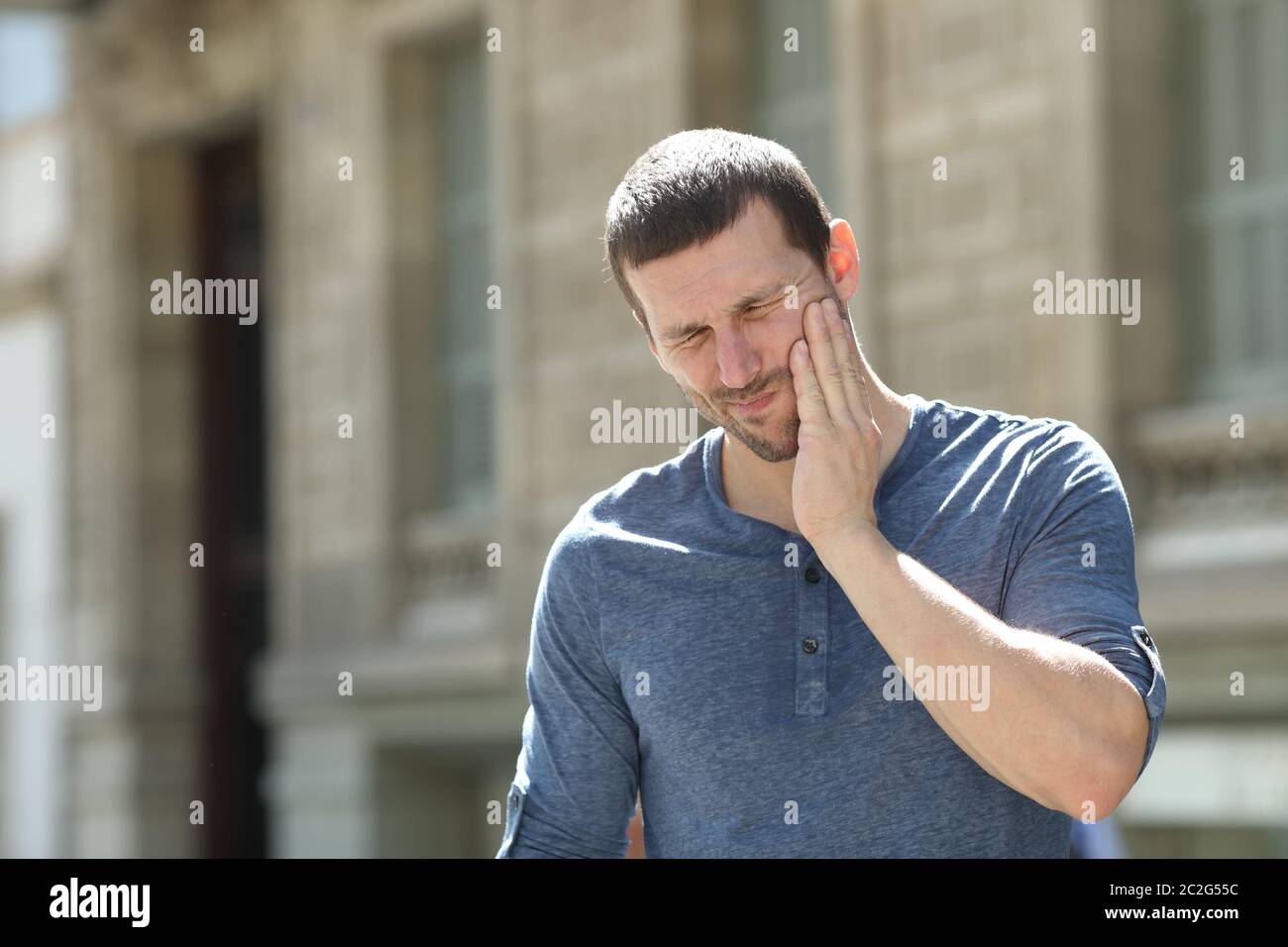 Stressed man suffering tooth ache standing alone in the street Stock Photo