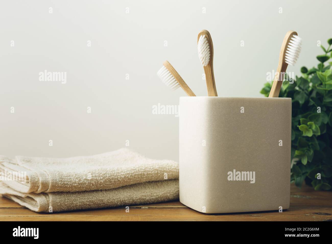 Three bamboo toothbrushes in a glass with plant and towerls an a background. Environmental awareness and oral care concept Stock Photo