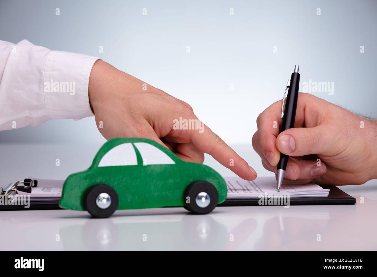 Close-up Of Man's Hand Signing Sales Contract For Car At Dealership Against Gray Background Stock Photo