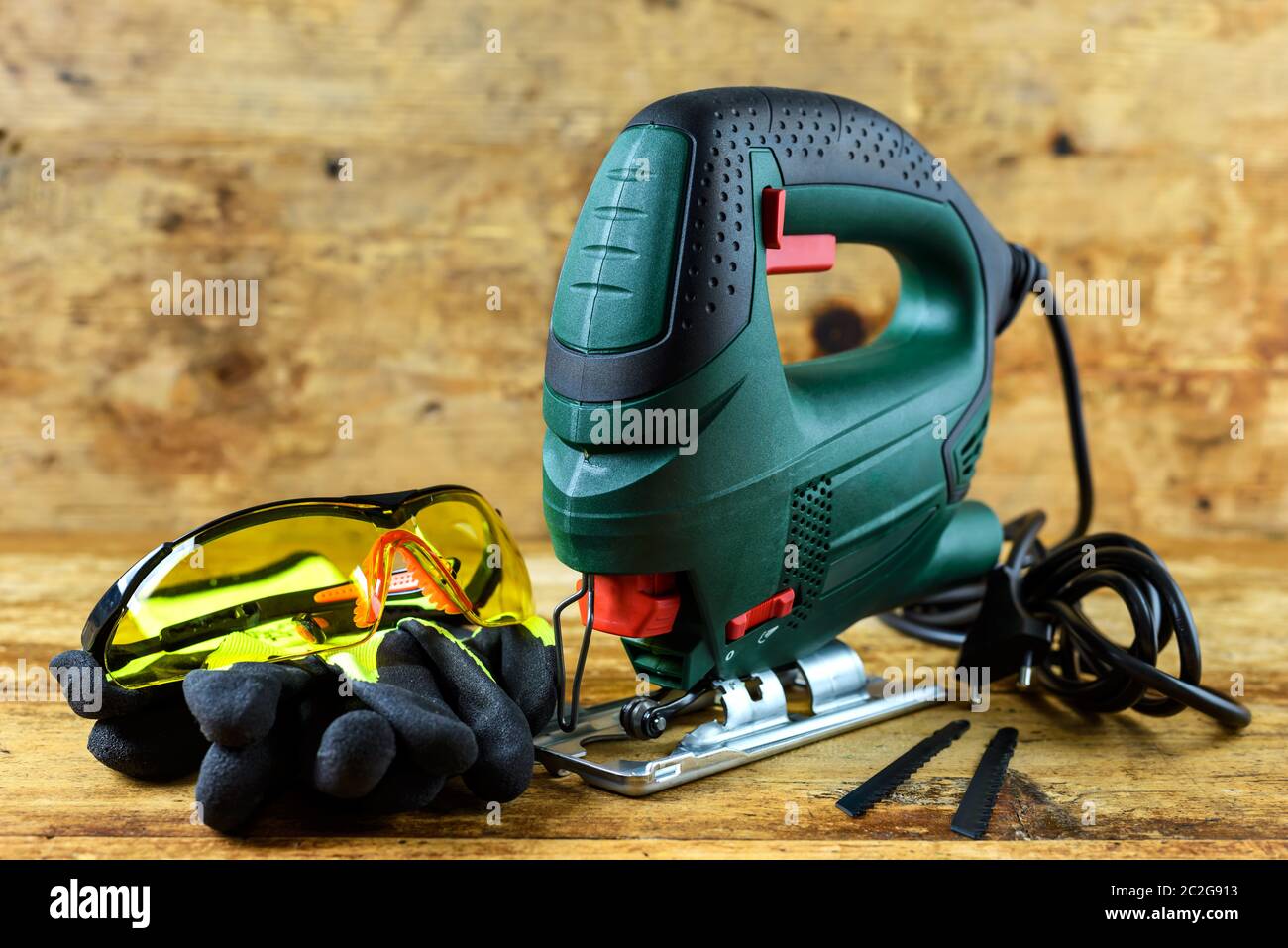 A jigsaw power tool, protective glasses, gloves and blades for electric jigsaw on vintage wooden background. Stock Photo